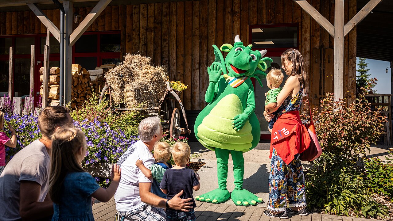 Eltern mit ihren Kindern winken Maskottchen, welches als grüner Drache verkleidet ist